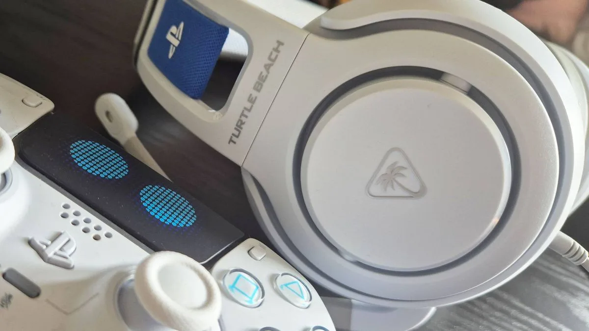 Photo of the Astro Bot PS5 controller on the bottom left, with a close up of the side of the Atlas 200 headset, showing off the Turtle Beach logo on the cup.